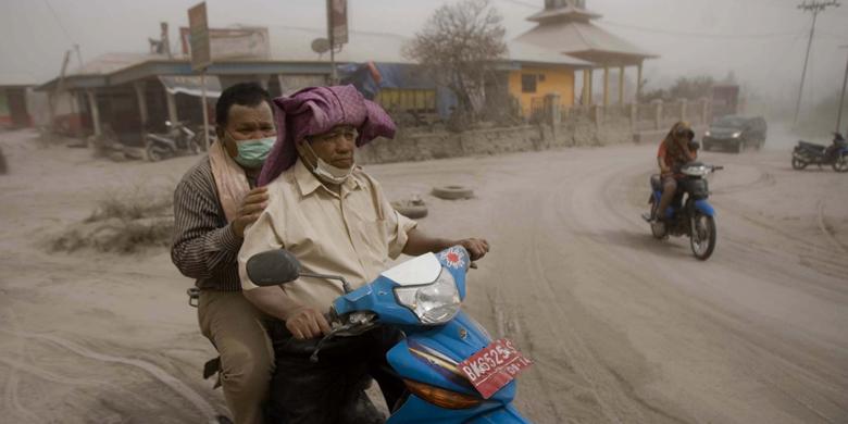 北スマトラ州カロ県シビントゥン村にてシナブン山噴火による火山灰の雨の中オートバイに乗る住民たち(1月16日)。